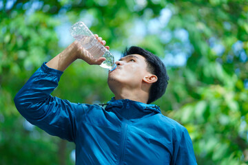 A man is drinking water from a bottle while wearing a blue jacket. Concept of staying hydrated and...