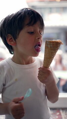 Young boy eating ice cream with a spoon and cone in hand, enjoying a sweet treat indoors, highlighting the joy of childhood indulgence in a casual setting