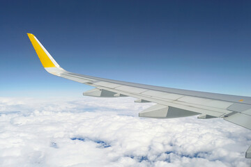 The wing of a large passenger plane flying above the clouds. The view seen from the plane window by tourists, migrants and people returning home from vacation.
