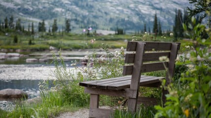 A photo of a wooden bench with greenery around it. The bench is placed near a body of water with rocks. There are wildflowers in full bloom near the bench. The background reveals a mountain