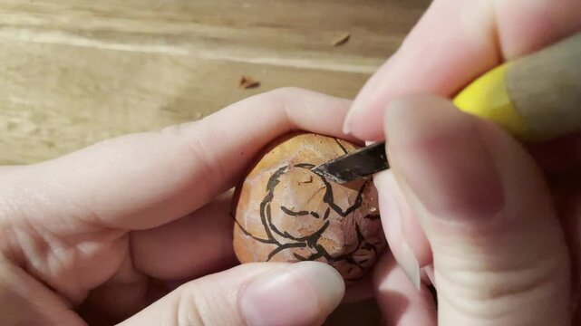 Closeup of a woman&rsquo;s hand carving in wood with a tiny knife, making a wooden figure
