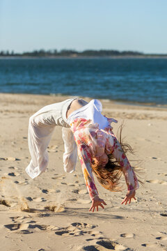 Teenaged First Nations Australian girl doing flips on sand at beach