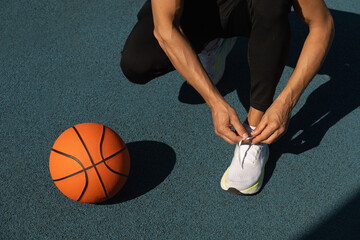 Close up basketball player tying sports shoes in basketball court outdoors. Last preparation. Summer team game.