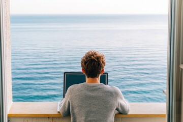 Fototapeta premium Person working on laptop with sea view from a balcony.