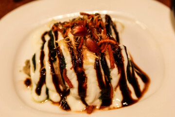 close up of Indian food Dilli Dahi Chaat which is popular street food is made with crispy papdi, sev and yoghurt on a white plate with sweet and sour taste