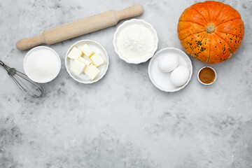 Baking ingredients including flour, butter, sugar, spices, eggs and pumpkin arranged on a gray background. Seasonal autumn baking