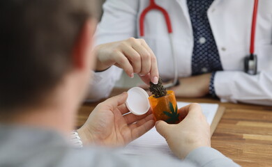 Close-up of doctor give bottle with dried cannabis to patient for health treatment. Man on appointment in hospital. Alternative medicine, health concept