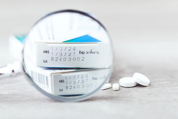 Close-up of the production code and expiration date printed on the side of a medicine box, with pills placed on a table. The image highlights the importance of checking medication before consumption