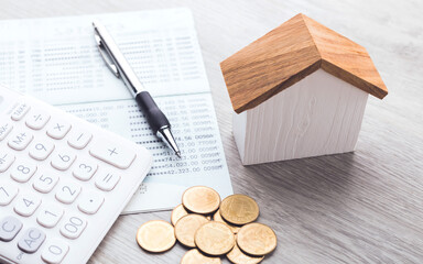 House model, coin pile, calculator, and savings account passbook are placed on the table,...