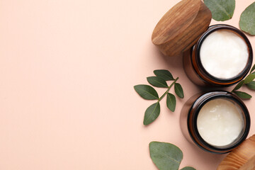 Different cosmetic products and green leaves on beige background, flat lay. Space for text