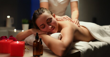 Portrait of young woman enjoying being massaged by professional masseuse master. Chilling female get body treatment in spa, candles and oils. Care concept