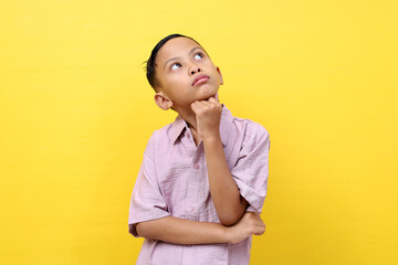 Thoughtful asian boy standing while looking up. Isolated on yellow background with copyspace