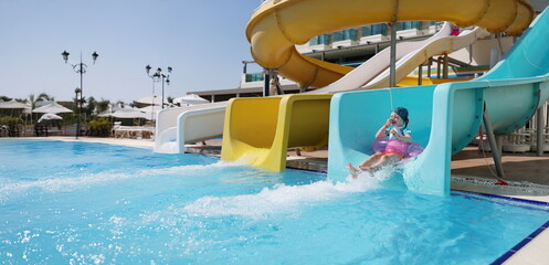 Portrait of happy little girl kid slide down hill on pink air mattress in water park. Smiling child...