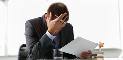 Close-up of adult man businessman hold paper sheet in hand and close face with palm. Wrong...
