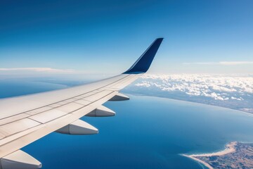 Obraz premium Airplane wing over ocean with clear blue sky and fluffy clouds.