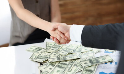 Close-up of man and woman shake hands over stack of dollars currency transaction of powers. People...