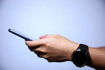 Closeup of hand holding or using smartphone on blue background.