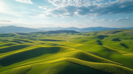 Obraz premium Rolling green hills under a partly cloudy sky in a picturesque rural landscape during late afternoon light