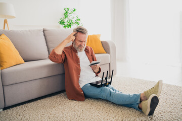 Full length photo of pensioner man sit floor confused read instruction wifi router dressed brown...