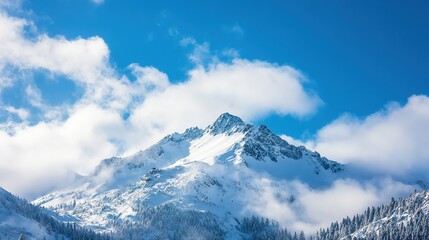 Obraz premium Majestic snow-capped mountain towering above fluffy clouds under a bright blue sky in a serene landscape