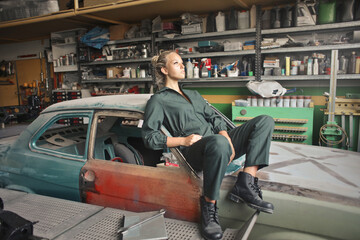female mechanic sitting on a car body in a garage