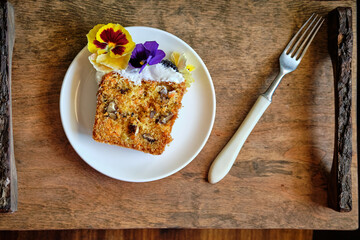 a piece of carrot sweet bread with walnuts, decorated with cream and edible flowers.