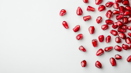 Scattered pomegranate seeds against a clean white background, creating a vibrant contrast with their rich red color, evoking freshness and health.