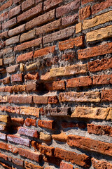 Brick wall and historic house facade in Pompeii, the Roman city near Naples in Italy that was destroyed by the Vesuvius volcano. Rows of irregular bricks in shades of red and orange in the contrasting