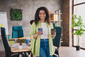 Photo of nice young woman office worker use smart phone drink coffee wear shirt loft interior business center indoors
