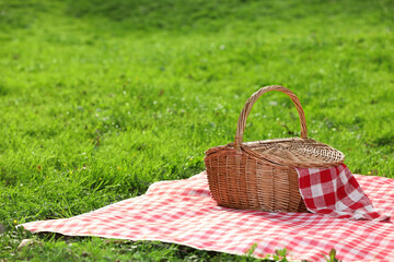 One picnic wicker basket with checkered napkin and blanket on green grass. Space for text