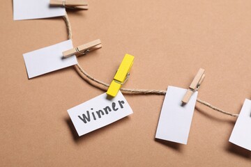 Paper note with word Winner among blank ones on rope against beige background, closeup
