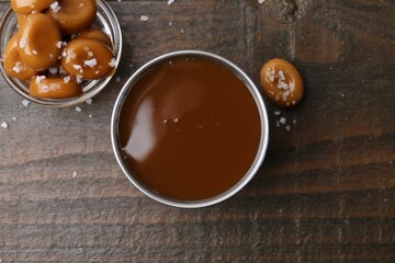 Tasty salted caramel in bowl and candies on wooden table, top view