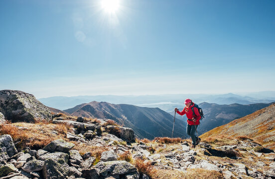 Backpacker woman in bright red jacket walking by mountain range using trekking poles with Liptov valley background, Western Tatras, Slovakia. Active people and European hiking tourism concept image. - Powered by Adobe