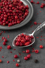 Pink peppercorn pepper berry  on retro metallic spoon closeup and on plate with crumbs on grey stone table background. Aromatic spicy ingredient for cuisine.