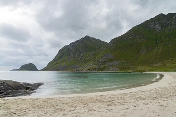 Sandy beach with stones and mountains in cloudy background, Lofoten Norway