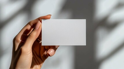 A Hand Holding a Blank White Card Against a Blurred Background