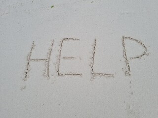 Distress message written in the sand at a beach, signaling for help during the day, with clear, sunny weather