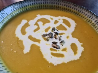 Pumpkin soup garnished with cream and pumpkin seeds served in a decorative bowl