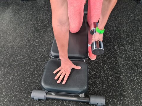 A person performs a single-arm dumbbell row on a weight bench in a gym during a strength training session