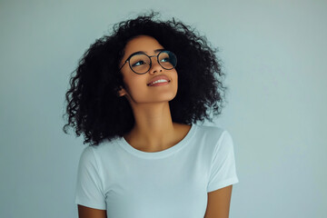Cute, smiling young woman with curly black hair, glasses, and a white t-shirt.