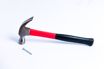 Close up a nail and medium sized hammer that has two functions as a nail pick and nail hammer, with a handle covered in black and red rubber isolated on a white background. Little bit rusty