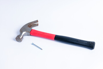 Close up a nail and medium sized hammer that has two functions as a nail pick and nail hammer, with a handle covered in black and red rubber isolated on a white background. Little bit rusty