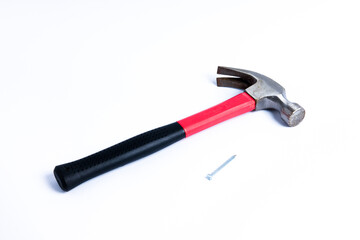 Close up a nail and medium sized hammer that has two functions as a nail pick and nail hammer, with a handle covered in black and red rubber isolated on a white background. Little bit rusty