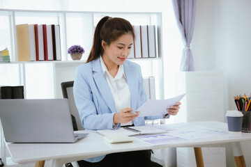 Confident and charming Asian businesswoman using laptop and smartphone. She is full of professionalism and achievement in data analysis, effective communication and organizational management in modern