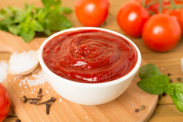 Delicious ketchup with spices and tomatoes on wooden table