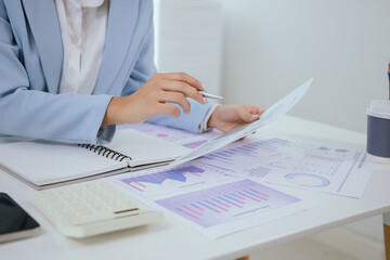 Confident Asian businesswoman in modern office smiling while working on laptop, analyzing reports, planning marketing strategies and leading with energy and positivity.