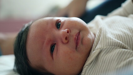 Close-up of a baby's face lying on a bed, gazing with wide, curious eyes. baby has soft expressions and the background is softly blurred, highlighting the baby in a cozy home setting