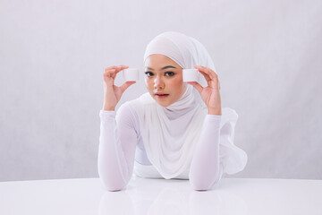 Gesture Beautiful young woman hijab sharp look at camera both hands hold cosmetic cream in front of face to show skin care products on white background. Commercial, health, medical and fashion concept