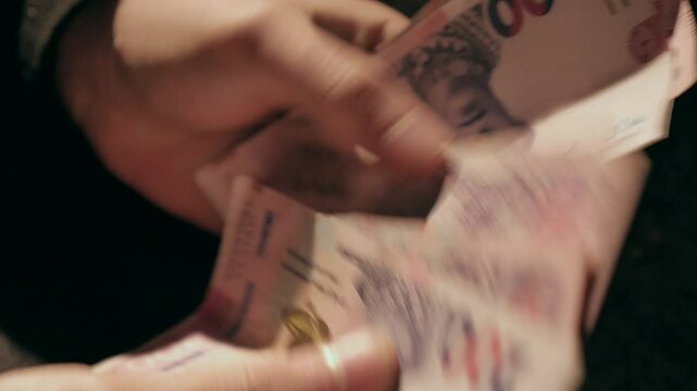 A close-up shot of a man's hands counting Ukrainian banknotes. The details of the bills, including the denomination and design of Ukraine's national currency, are clearly visible