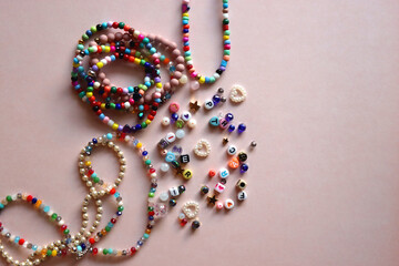 Colorful DIY necklaces, friendship bracelets and various plastic beads on pastel pink background....